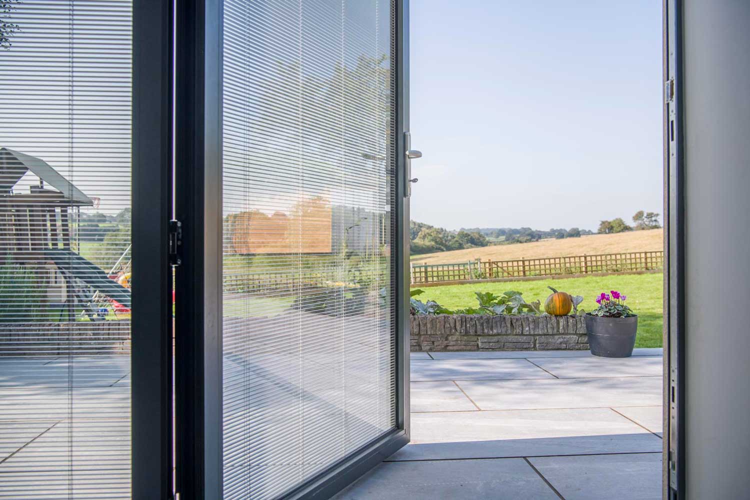 Blinds in Glass in Baldock: integral blinds in open bifold doors with a countryside view